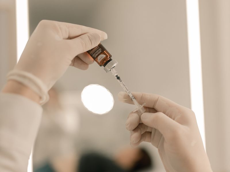 Gloved hands drawing serum into a syringe in a softly lit clinical setting